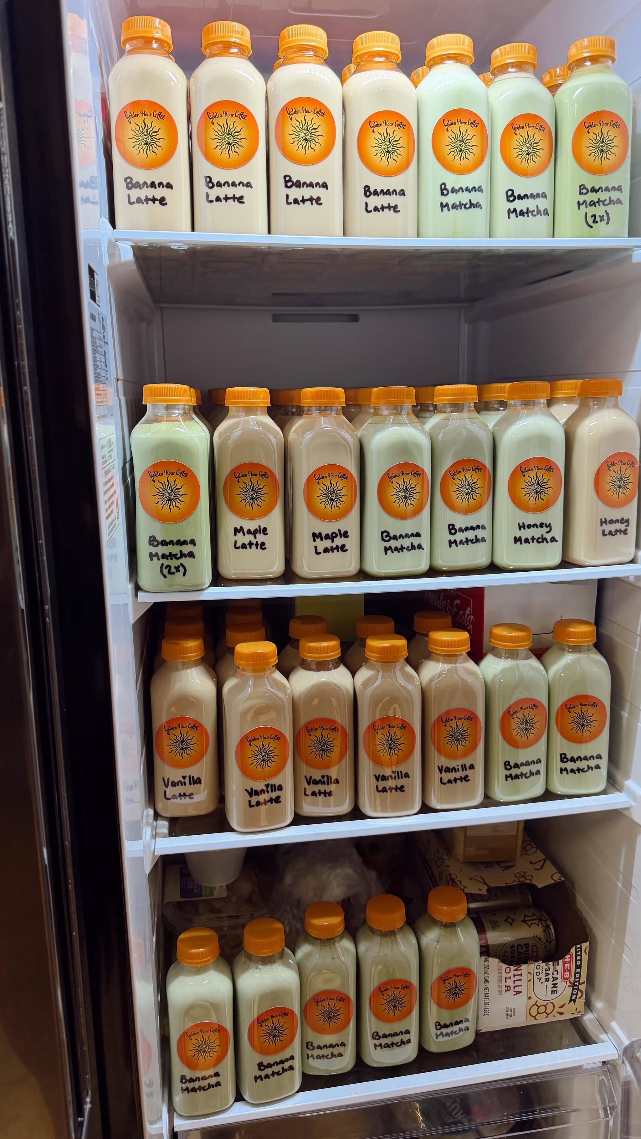 A cart fridge stocked with rows of hand-labeled Golden Hour bottles: Banana Latte, Maple Latte, Vanilla Latte and more.